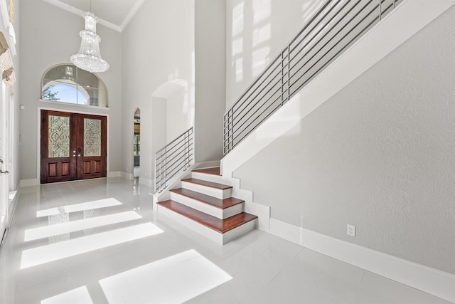 foyer entrance featuring a high ceiling, french doors, an inviting chandelier, light tile patterned floors, and crown molding