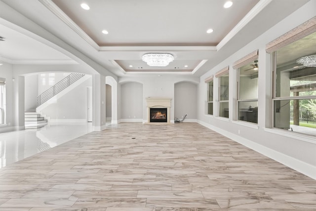 unfurnished living room with ceiling fan, a tray ceiling, and ornamental molding