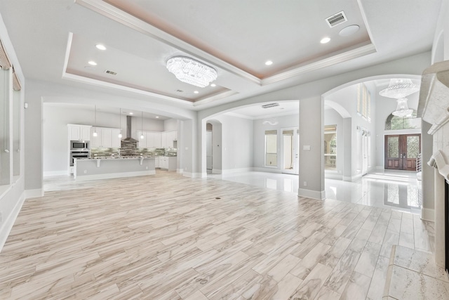 unfurnished living room featuring a raised ceiling, french doors, crown molding, and an inviting chandelier