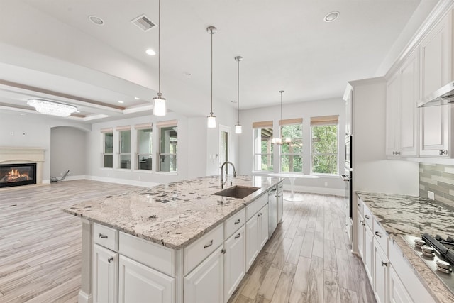 kitchen with white cabinetry, an island with sink, decorative backsplash, hanging light fixtures, and sink