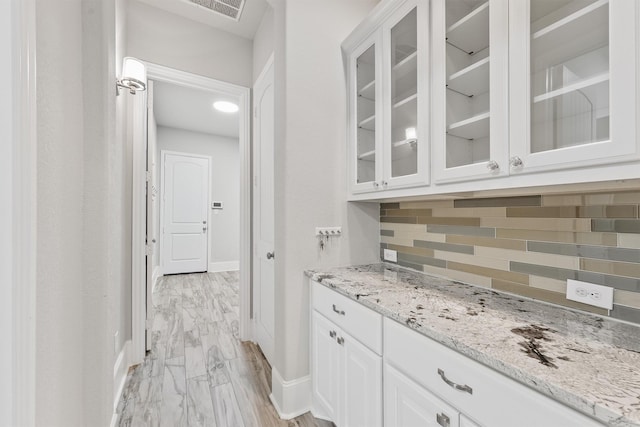 bar featuring white cabinets, backsplash, and light stone counters