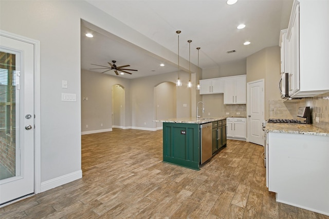 kitchen with tasteful backsplash, arched walkways, white cabinets, appliances with stainless steel finishes, and a sink