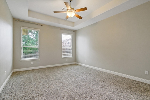 carpeted spare room with ceiling fan, a raised ceiling, and baseboards