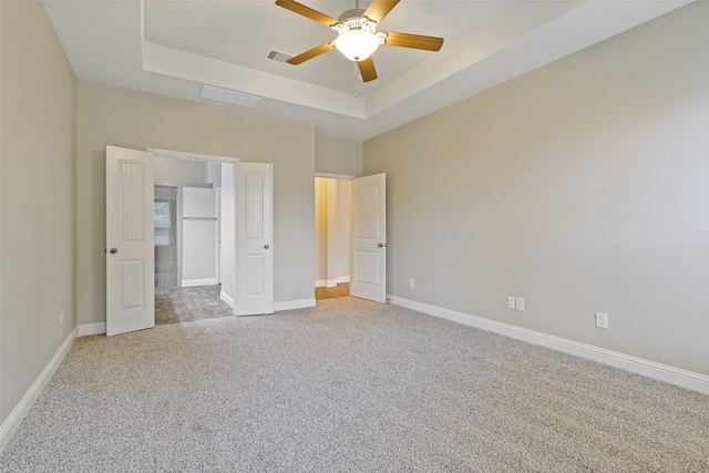 unfurnished bedroom featuring light carpet, baseboards, visible vents, freestanding refrigerator, and a tray ceiling