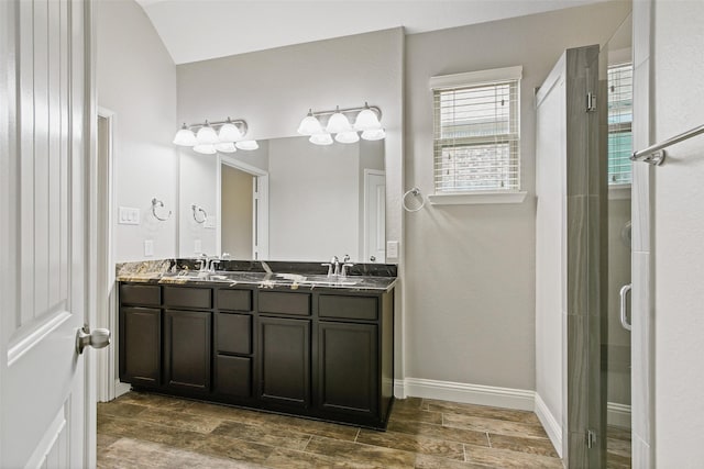 bathroom with double vanity, a stall shower, baseboards, wood tiled floor, and a sink