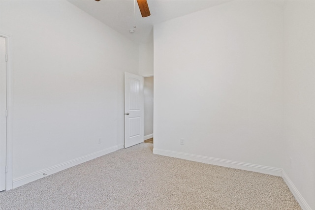 spare room with light carpet, ceiling fan, a towering ceiling, and baseboards