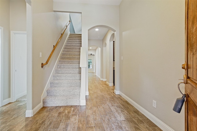 stairway with arched walkways, recessed lighting, baseboards, and wood finished floors