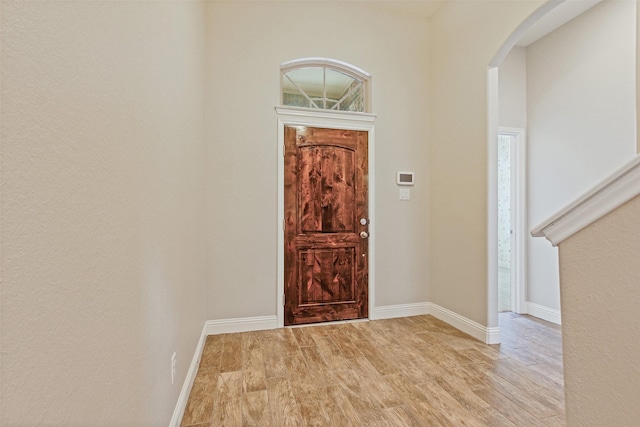 foyer featuring arched walkways, baseboards, and light wood-style floors