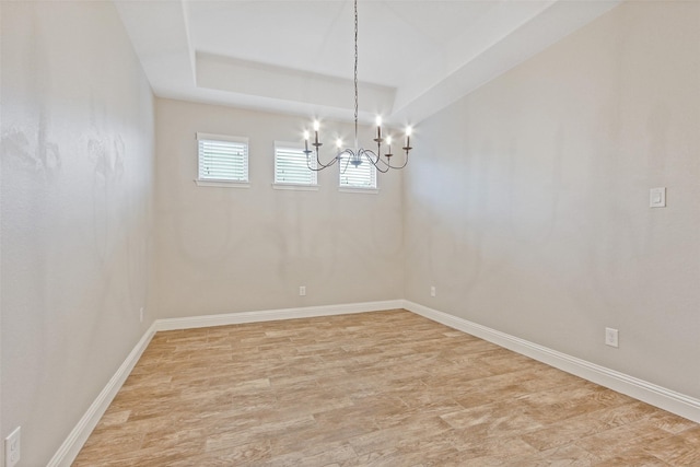 unfurnished room with light wood-style floors, a chandelier, a raised ceiling, and baseboards