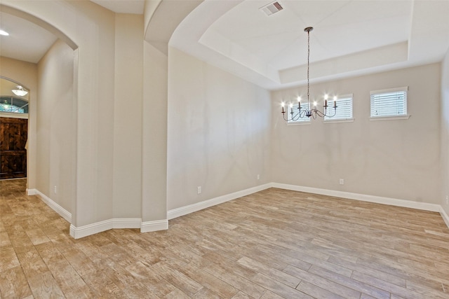 empty room with light wood-type flooring, a tray ceiling, and arched walkways