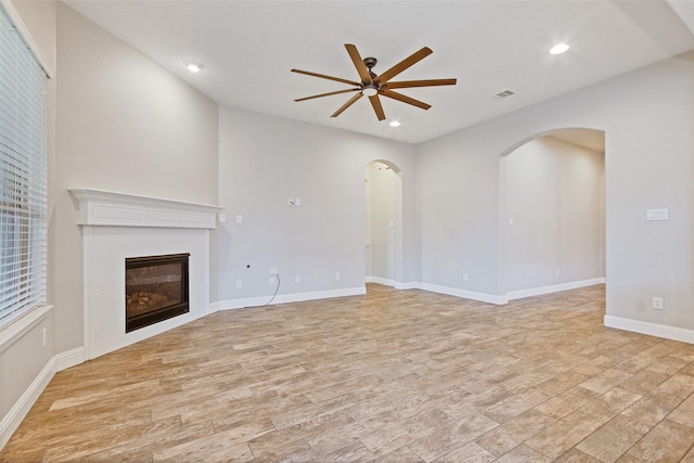 unfurnished living room featuring arched walkways, ceiling fan, recessed lighting, visible vents, and a glass covered fireplace