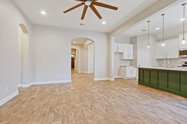 unfurnished living room featuring arched walkways, ceiling fan, visible vents, baseboards, and light wood-style floors