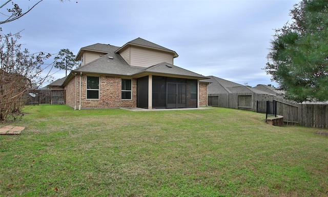 back of property featuring a shingled roof, a lawn, a sunroom, a fenced backyard, and brick siding