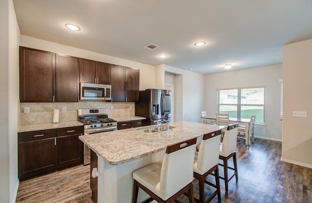 kitchen with dark brown cabinetry, appliances with stainless steel finishes, sink, a breakfast bar, and a center island with sink