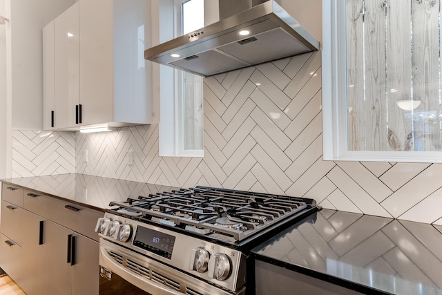 kitchen with tasteful backsplash, extractor fan, dark stone countertops, stainless steel gas range oven, and white cabinetry