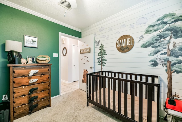 bedroom featuring a textured ceiling, light carpet, ornamental molding, ceiling fan, and a nursery area