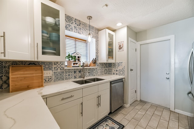 kitchen with pendant lighting, stainless steel dishwasher, sink, a textured ceiling, and light stone counters