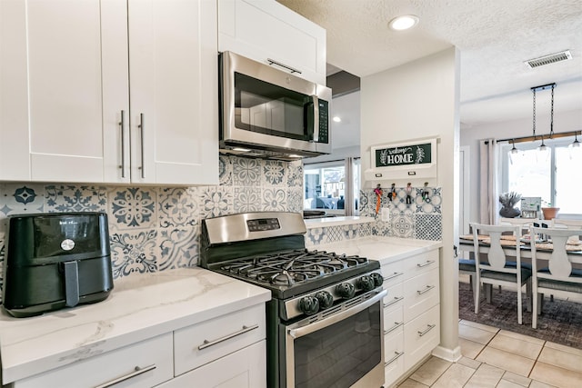 kitchen featuring light tile patterned floors, white cabinetry, appliances with stainless steel finishes, a textured ceiling, and light stone counters