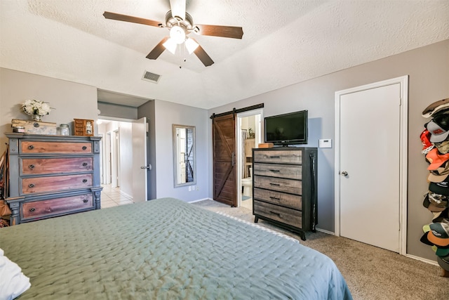 bedroom featuring a textured ceiling, ceiling fan, a barn door, and light colored carpet