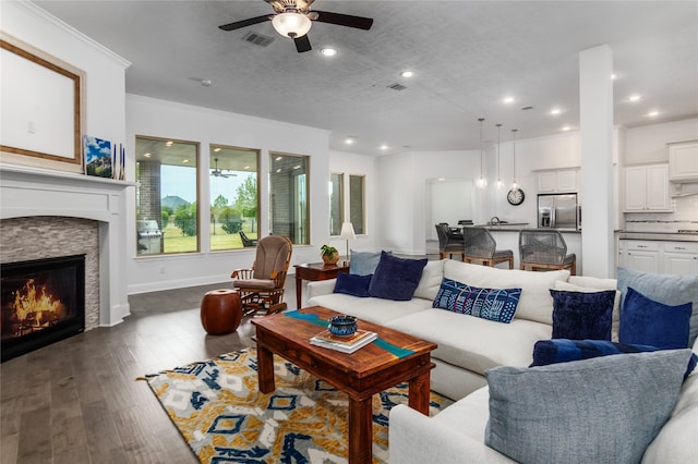 living room featuring a textured ceiling, ceiling fan, dark hardwood / wood-style floors, and a stone fireplace