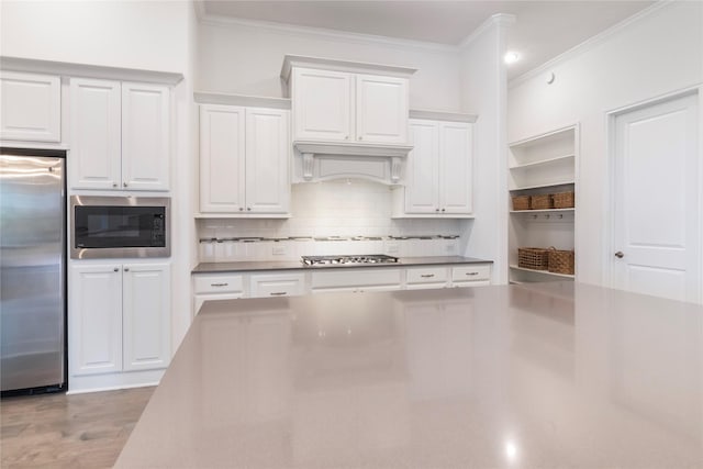 kitchen with appliances with stainless steel finishes, custom exhaust hood, white cabinetry, ornamental molding, and light wood-type flooring