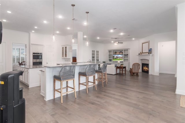 kitchen featuring ceiling fan, a large island with sink, pendant lighting, a breakfast bar, and white cabinetry