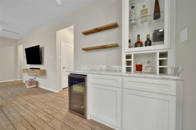 bar with beverage cooler, white cabinets, and light stone counters