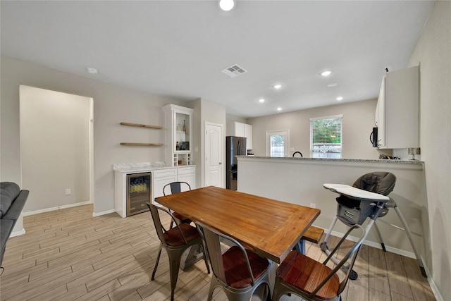 dining space with beverage cooler and light hardwood / wood-style flooring