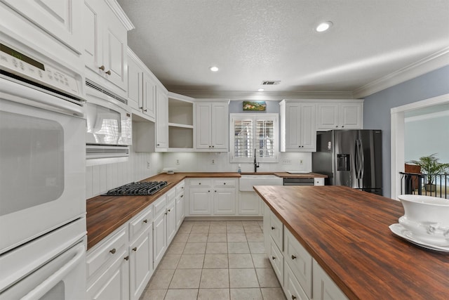 kitchen with appliances with stainless steel finishes, white cabinets, and butcher block countertops