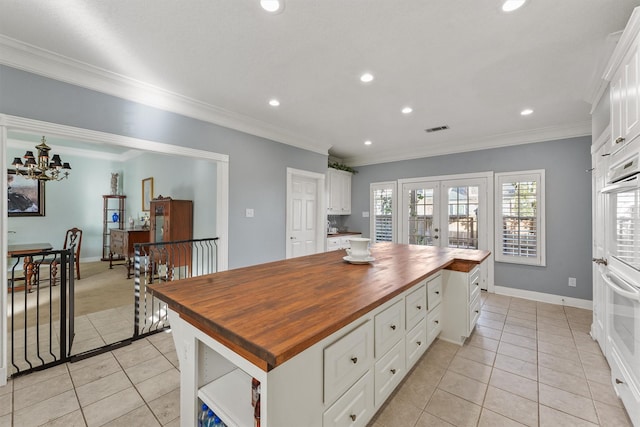 kitchen with butcher block countertops, light tile patterned floors, white cabinetry, and a kitchen island