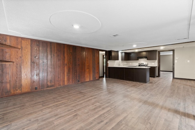 kitchen with stainless steel electric stove, wood walls, dark brown cabinetry, and sink