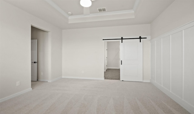 unfurnished room with a barn door, a tray ceiling, and light colored carpet