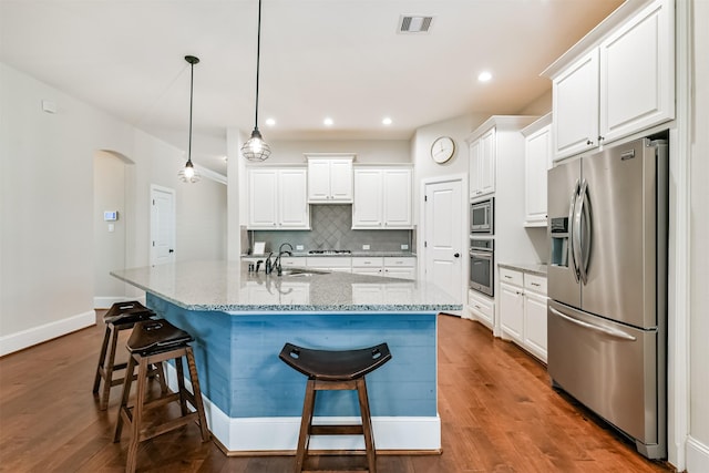 kitchen featuring stainless steel appliances, pendant lighting, white cabinets, and an island with sink