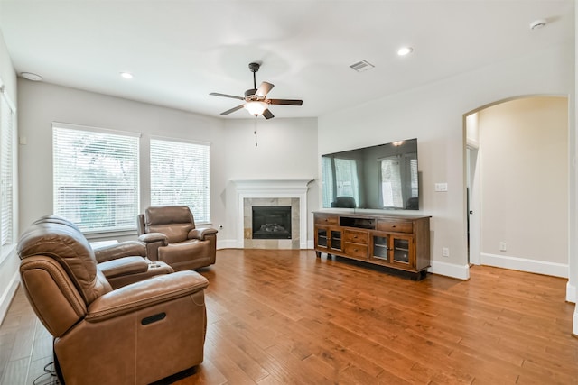 living room featuring light wood-type flooring, ceiling fan, and a tiled fireplace