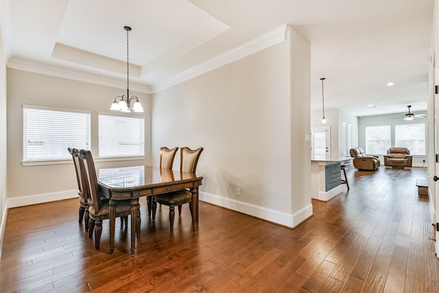 dining area with ceiling fan with notable chandelier, dark wood-type flooring, crown molding, and a raised ceiling