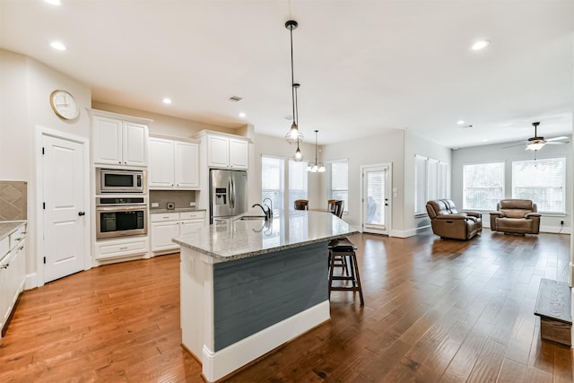 kitchen with decorative light fixtures, a kitchen island with sink, appliances with stainless steel finishes, and light stone counters