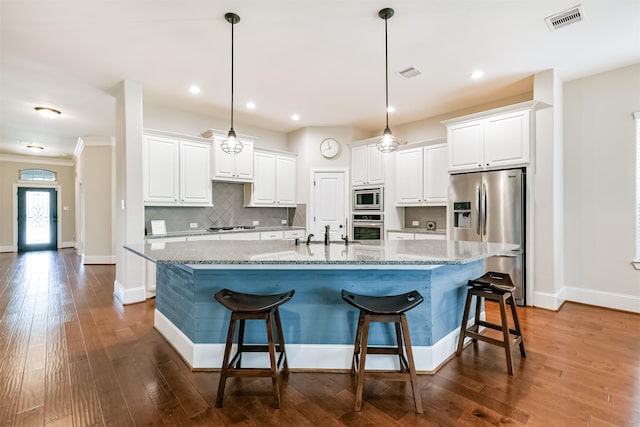 kitchen with a large island with sink, hanging light fixtures, light stone countertops, appliances with stainless steel finishes, and white cabinets