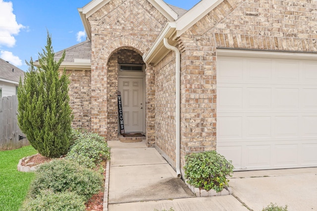 entrance to property with brick siding, an attached garage, and a shingled roof