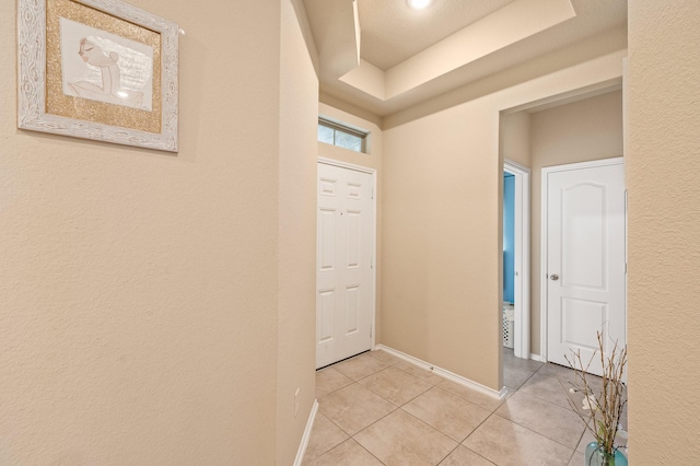 hall featuring light tile patterned flooring and a tray ceiling