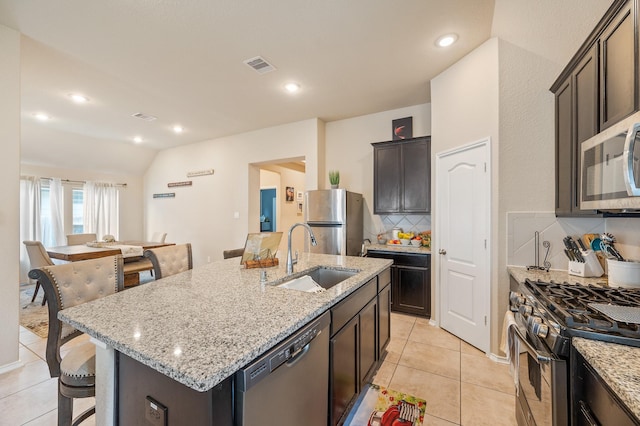 kitchen featuring appliances with stainless steel finishes, decorative backsplash, a kitchen island with sink, vaulted ceiling, and sink