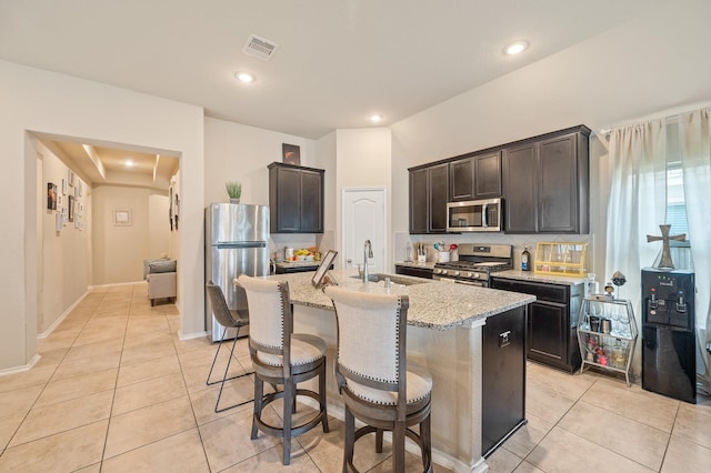 kitchen with light tile patterned floors, appliances with stainless steel finishes, a center island with sink, and sink