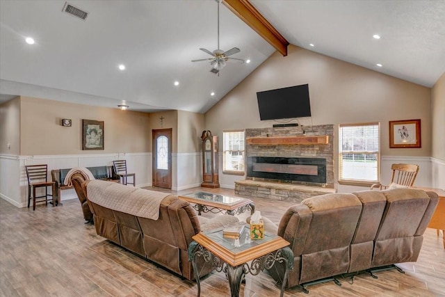 living room with beam ceiling, plenty of natural light, a stone fireplace, and light hardwood / wood-style flooring