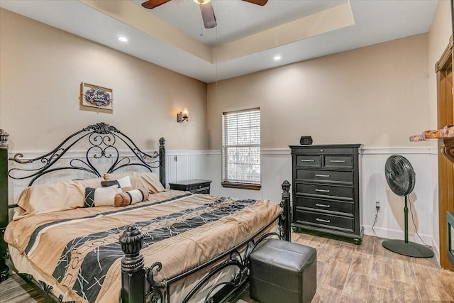 bedroom with ceiling fan, light hardwood / wood-style floors, and a tray ceiling