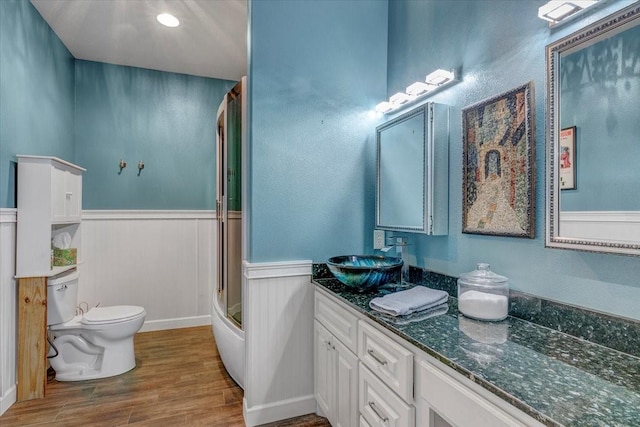 bathroom featuring toilet, vanity, wood-type flooring, and a shower with door