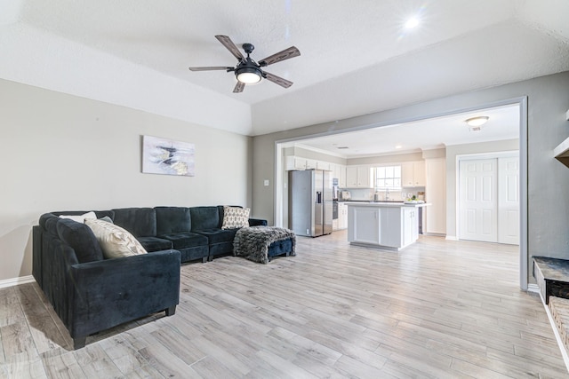 living room with a raised ceiling, light wood-type flooring, a textured ceiling, and ceiling fan