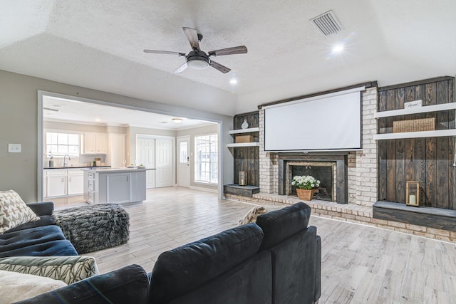 living room featuring a textured ceiling, a brick fireplace, a wealth of natural light, and light hardwood / wood-style flooring