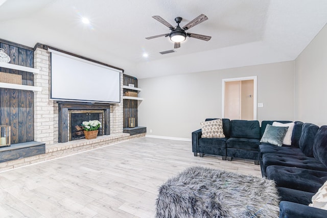 living room with ceiling fan, light wood-type flooring, a brick fireplace, and a tray ceiling