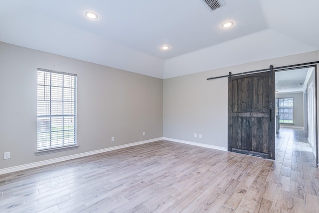 unfurnished room featuring light hardwood / wood-style floors, a raised ceiling, and a barn door