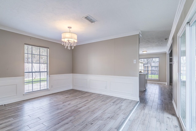 unfurnished room with a textured ceiling, an inviting chandelier, ornamental molding, and light hardwood / wood-style flooring