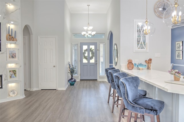 foyer entrance with light wood-type flooring, an inviting chandelier, crown molding, and a towering ceiling